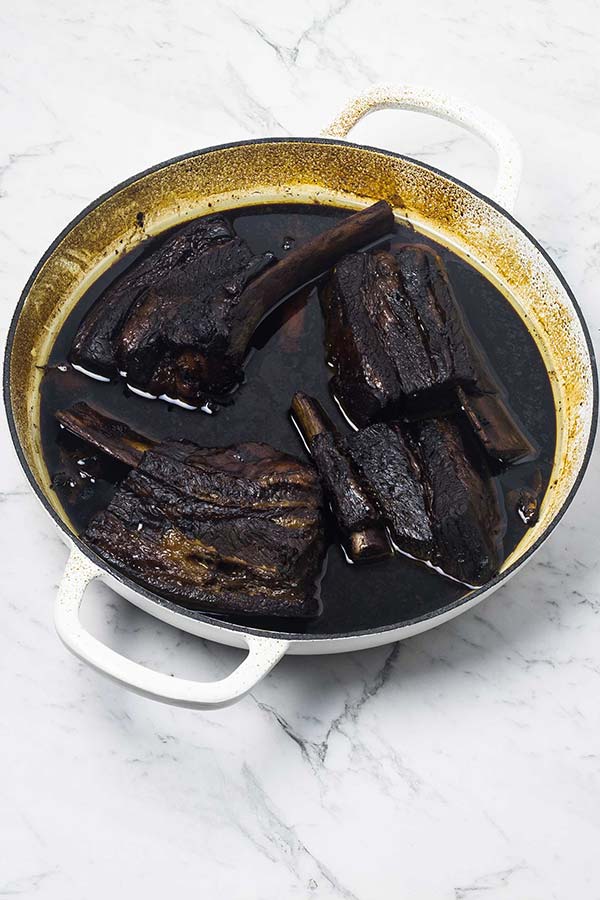 Steam oven baked sticky Asian beef ribs in a dark sauce in a white casserole dish