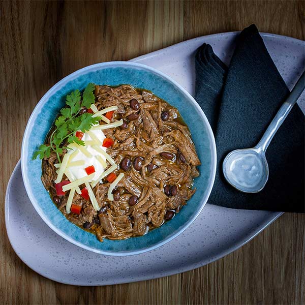 shredded meat and beans garnished with sour cream and other toppings in a blue bowl