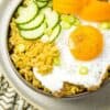 A zoomed in picture of seasoned rice topped with a seasoned fried egg, cucumber moons, pickled carrot and scallions