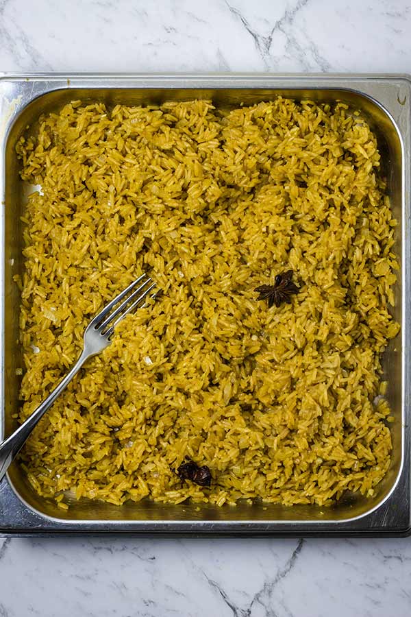 Rice being fluffed with a fork in a stainless steel pan