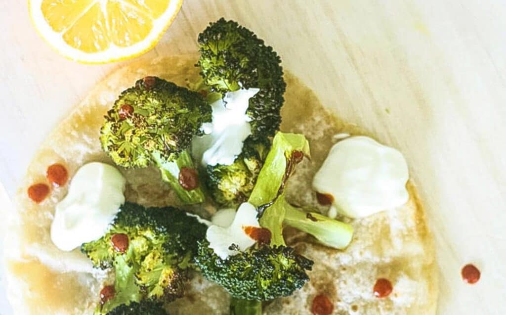 Steam oven lemon roasted broccoli florets on a pita bread with a halved lemon, white dressing and drops of chilli sauce
