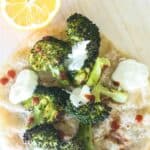 Lemon roasted broccoli cooked in a steam oven on a pita bread with a halved lemon, white dressing and red chilli sauce