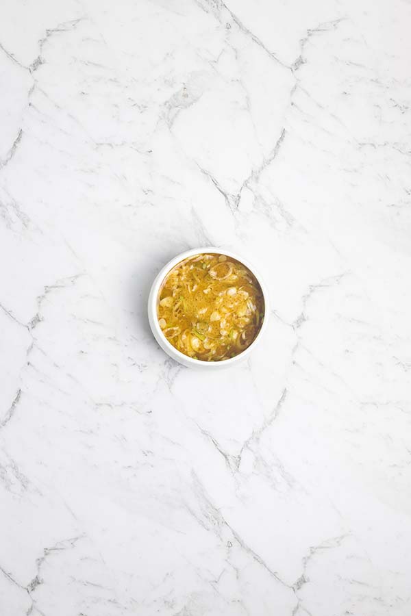 A white round bowl with miso dressing with sliced scallions