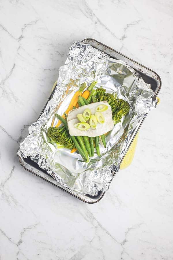 a rectangular baking tray covered in foil with fish and vegetables