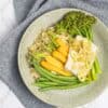 A speckled plate with steamed fish and vegetables on a grey linen teatowel