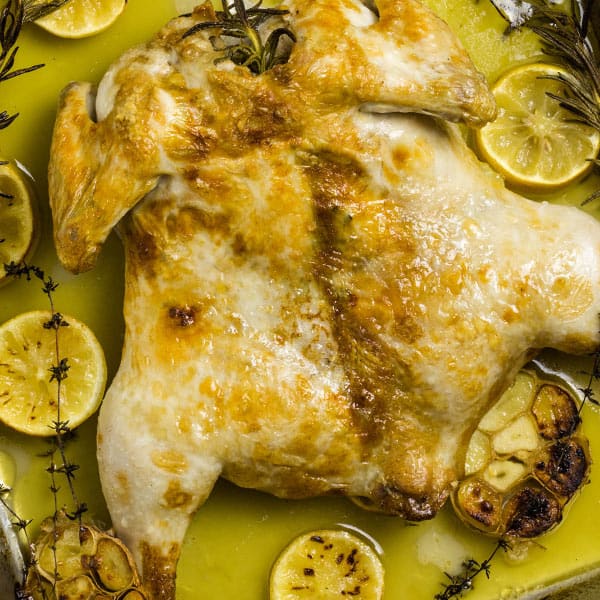 Butterflied roasted chicken surrounded by melted butter, and roasted lemon, garlic and herbs