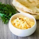 A small white bowl with fluffy, seasoned scrambled eggs in front of tortillas and a bunch of rocket.