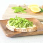 A piece of Pea and Fava Bean Crostini on a wooden plate
