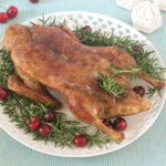 A round white platter with a combi steam roasted duck, on a striped cloth.