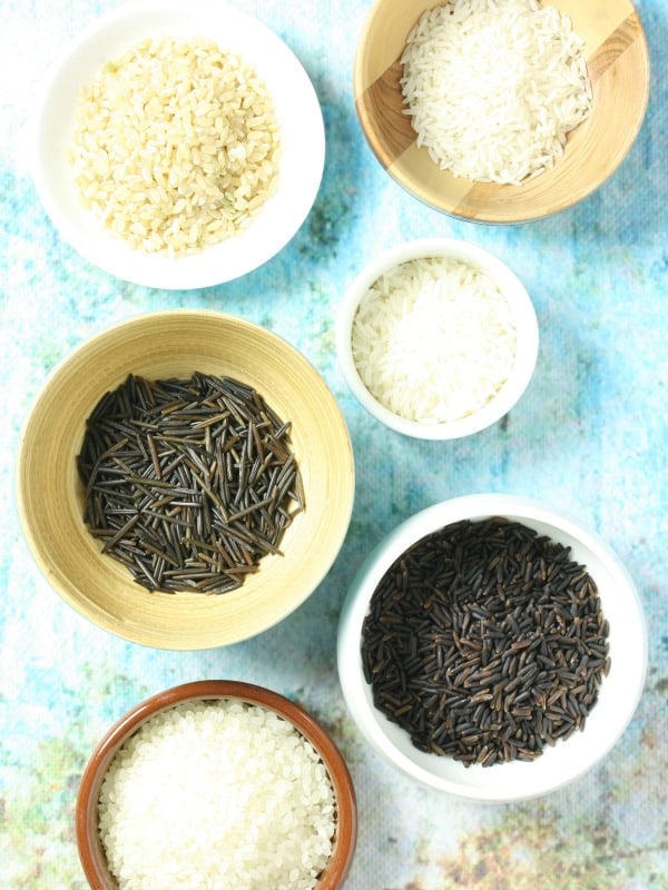 6 small bowls showing different varieties of rice, on a blue background, ready to make steam oven rice.