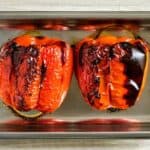 A silver baking tray with two whole roasted peppers