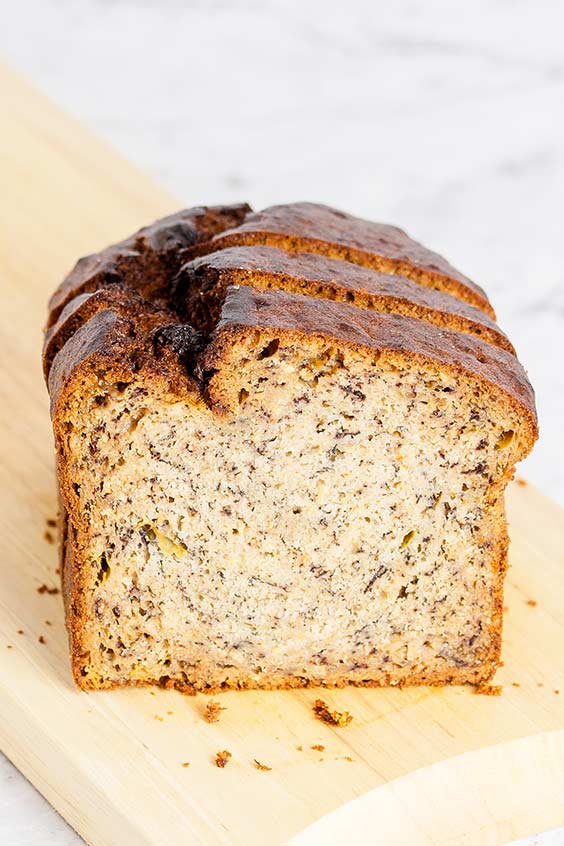 Slices of a loaf of banana bread on a wooden board on a marble counter