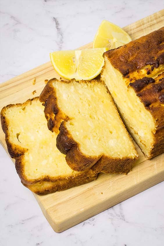 lemon ricotta cake, on a wooden board with two slices cut from the end of the loaf