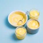 lemon curd in a white dish with a spoon that has been put into jars and a blue ramekin