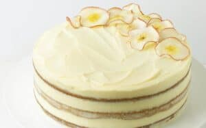 a triple layered apple spice cake with pale yellow frosting and decorative apple slices