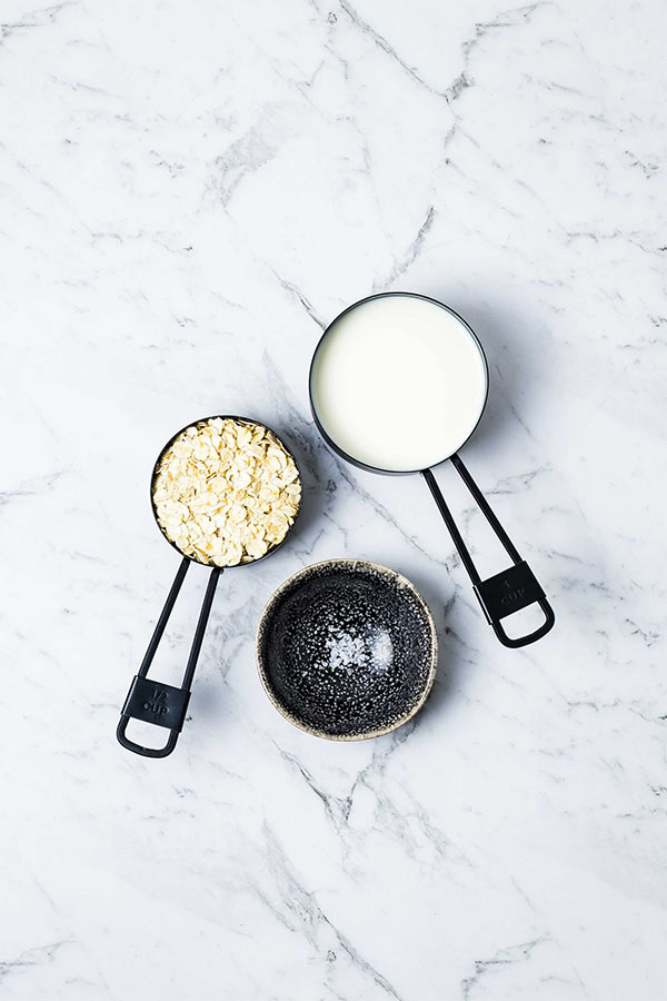 measuring cups with oats, milk and a small black dish with a pinch of salt