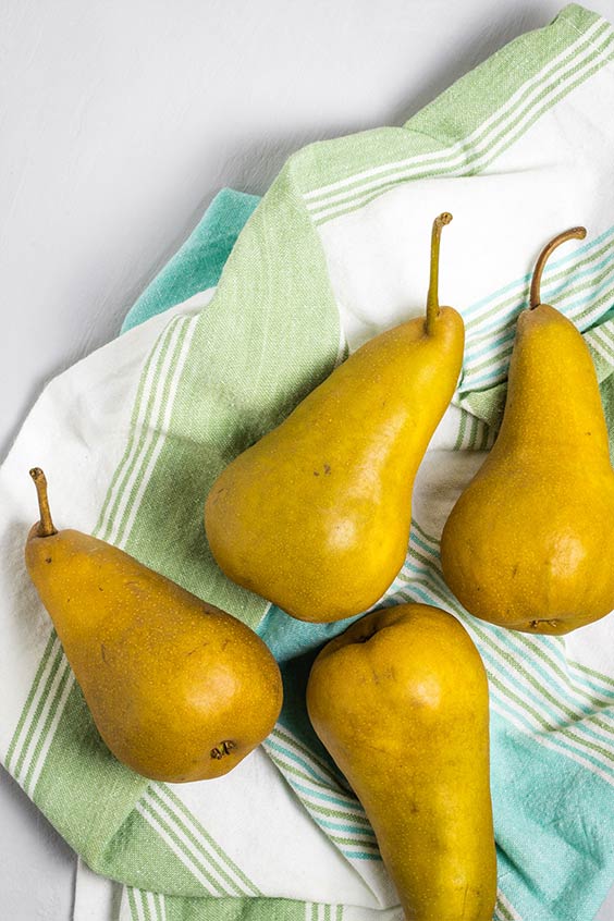 four ripe pears laid on a striped tea towel