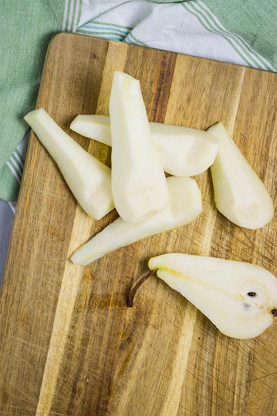 a wooden cutting board with a peeled and sliced pear, on a striped tea towel