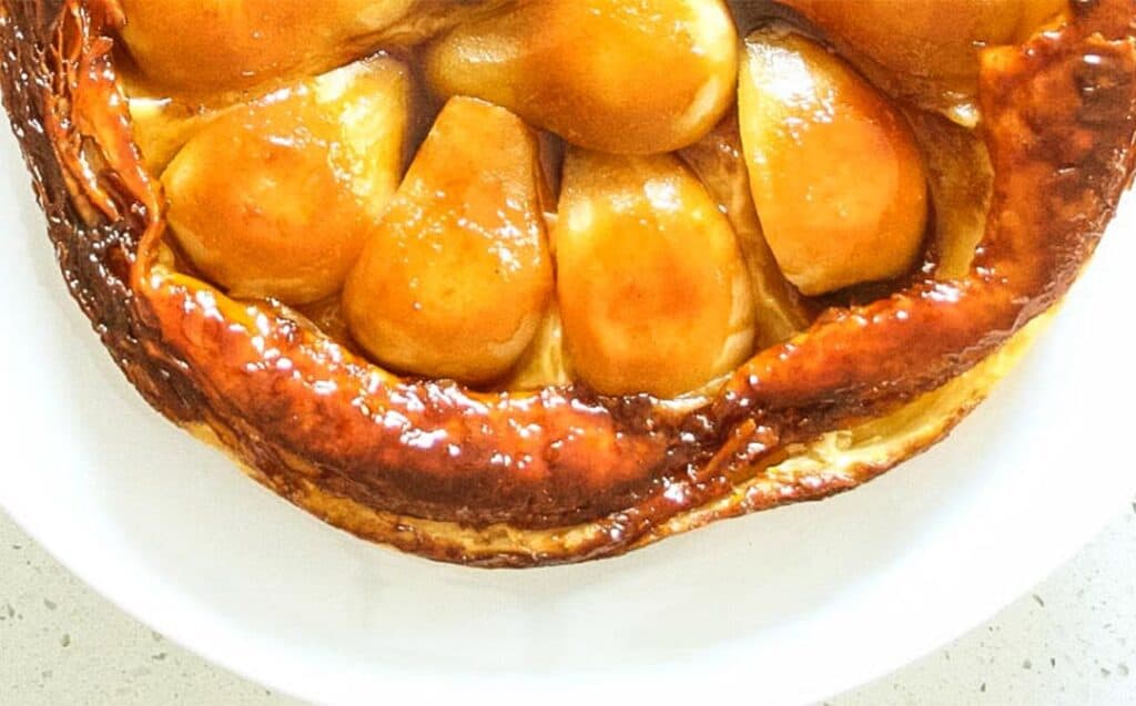 a close up image of golden apple pieces in a puff pastry shell on a white plate