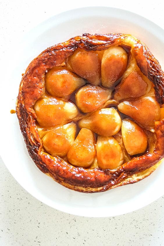 a puff pastry shell with golden apple pieces on a white plate on a speckled bench top