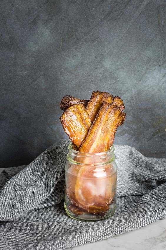 a glass jar with crispy combi steamed strips of bacon, with a grey cloth behind them