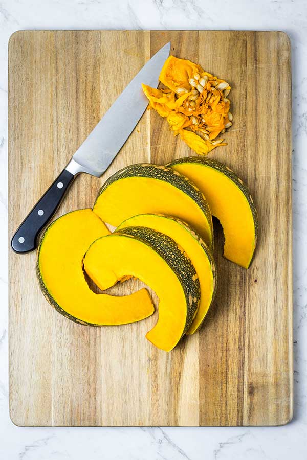 wooden board with wedges of pumpkin and a pile of scraped pumpkin seeds to the side