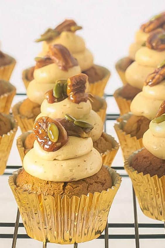 close up image of a row of pumpkin spice cupcakes with brown butter frosting, candied pecans and pumpkin seeds on top