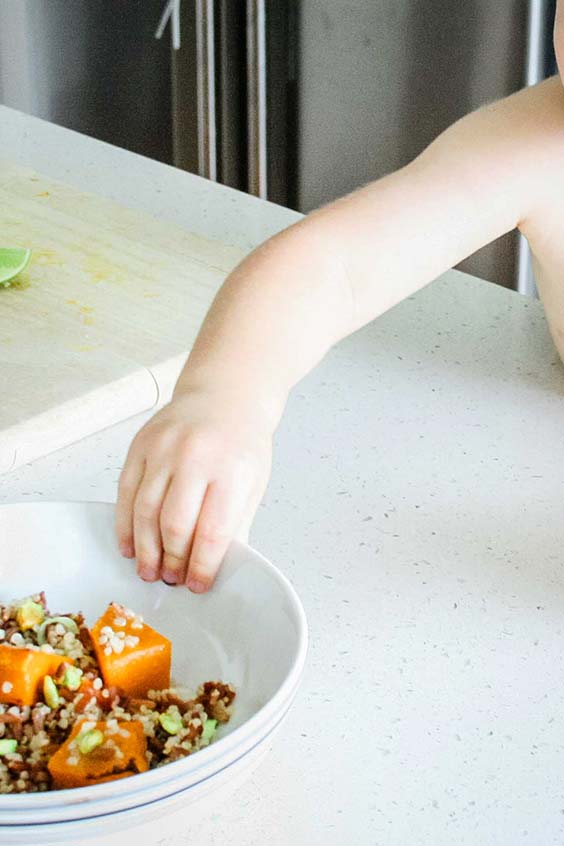 a child's hand grabbing a bowl of pumpkin and red rice salad