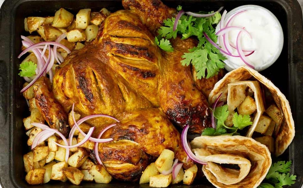 tandoori roast chicken in a baking dish with potatoes, red onion, yoghurt and flatbreads