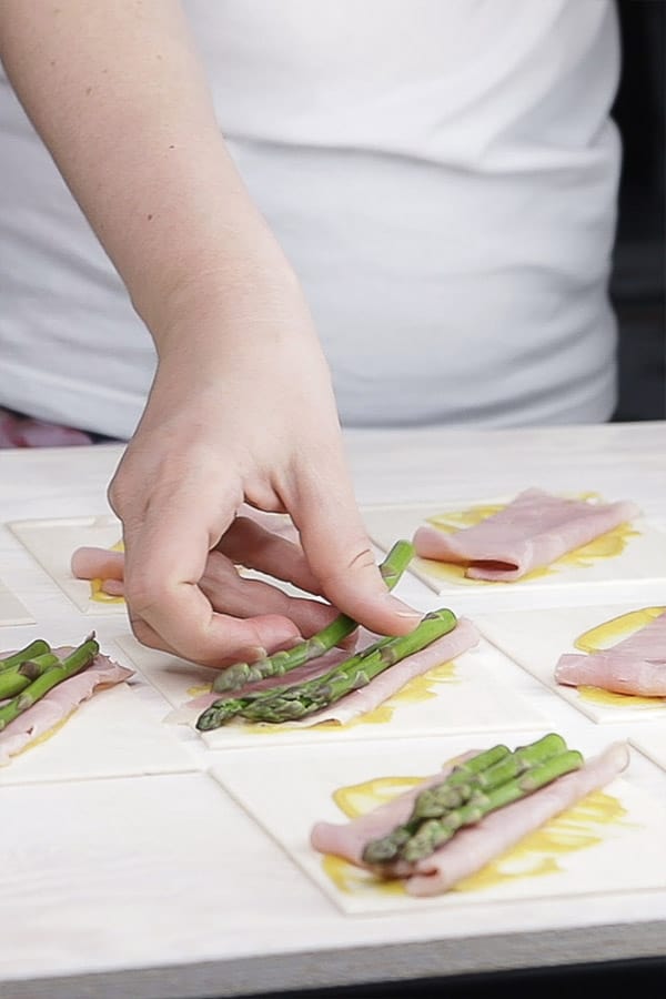 Asparagus spears being laid on top of folded ham and sauce on a piece of pastry