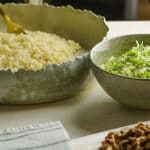 Rustic earthenware bowls with pearl couscous and shredded Brussels sprouts, alongside a dish with toasted pecans and dried cranberries.