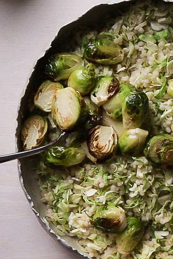An overhead view of a rustic salad bowl with roasted Brussels sprouts nestled on top of pearl couscous and shredded sprouts