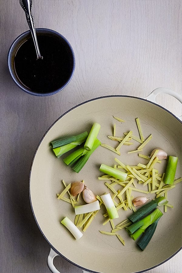 Chopped spring onions, garlic cloves and sticks of ginger in a white pan