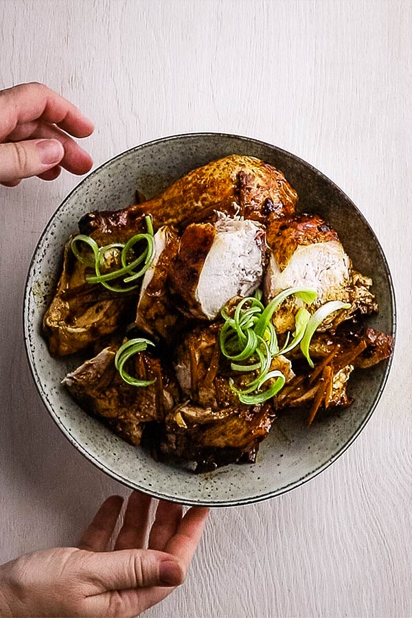 An overhead image of a serving dish with a whole chicken cut into pieces and garnished with spring onion curls