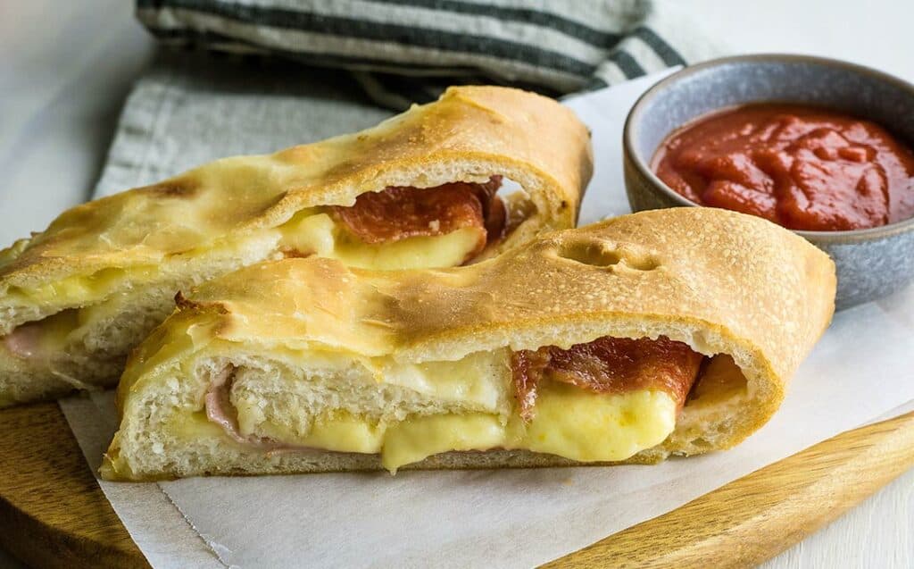 Two thick slices of meat and cheese filled stromboli on a board with a ramekin of sauce