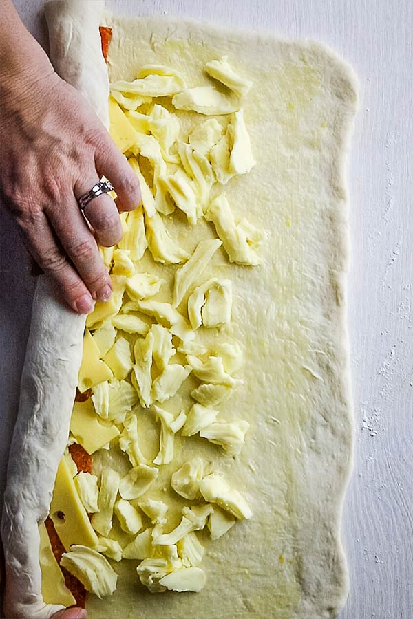 Rolling the long edge of the dough over the fillings to make Stromboli