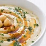 a white bowl with swirled hummus, parsley and paprika on top