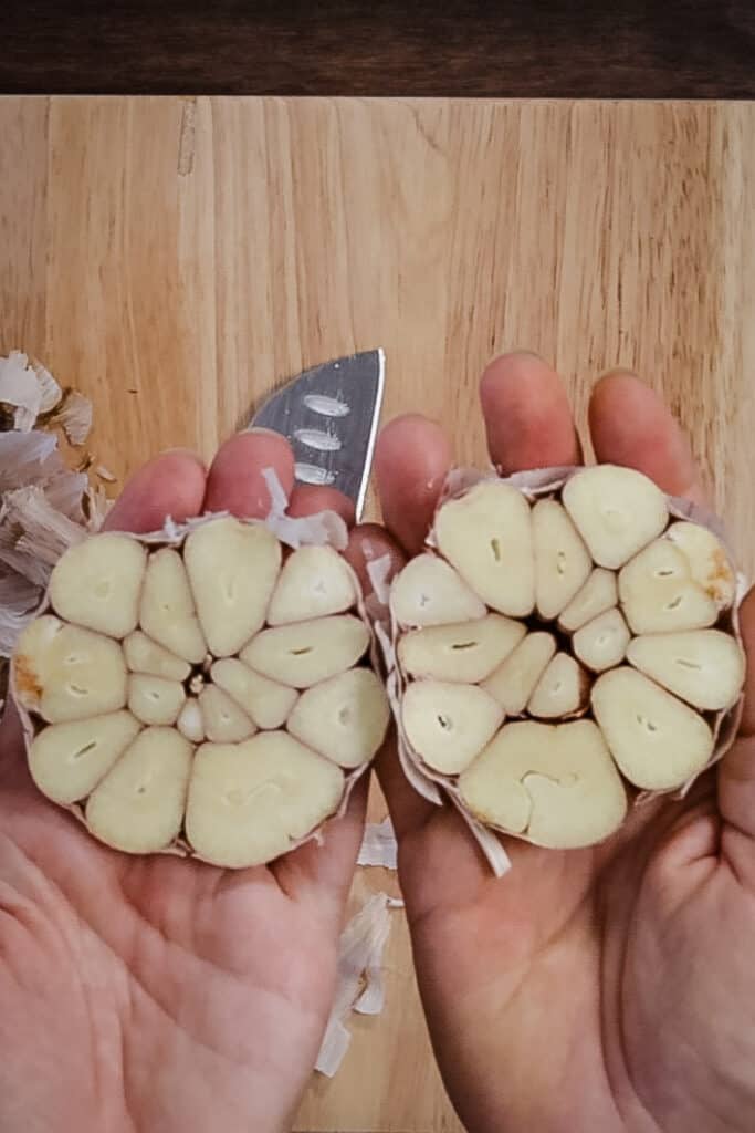 two hands hold a cut head of garlic up to the camera, with the cut sides facing upwards on the palms.