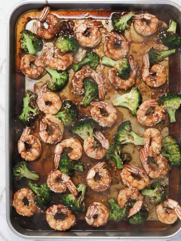 Freshly cooked shrimp and broccoli in soy, ginger and sesame sauce, sitting on a sheet pan.