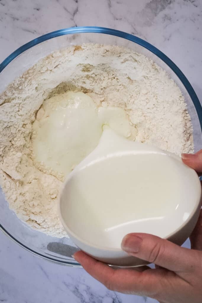milk pouring into a big clear glass bowl with flour