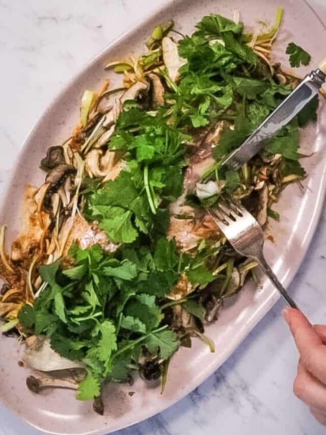 atop the marble counter is a white oval dish plate with Vietnamese steamed fish topped with cilantro