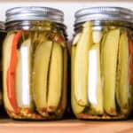 assorted pickled cucumbers in tall mason jars, on a wooden board.