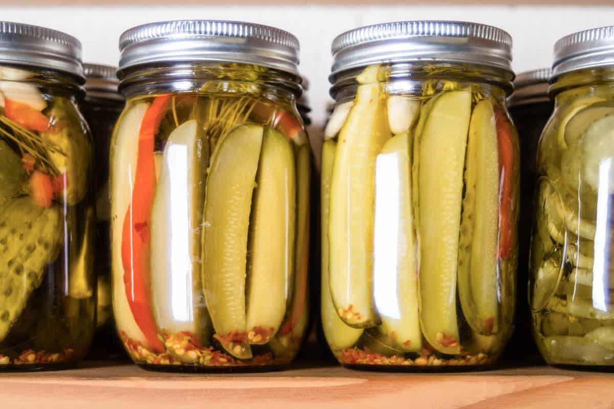 assorted pickled cucumbers in tall mason jars, on a wooden board.