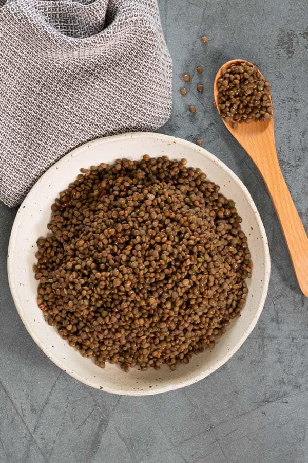 a white bowl of French puy lentils, with a wooden serving spoon alongside; showing how to steam lentils