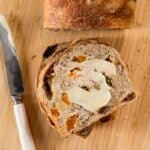 a slice of fruit and nut bread that's been baked in a steam oven, with a smear of butter across the surface and the butter knife alongside