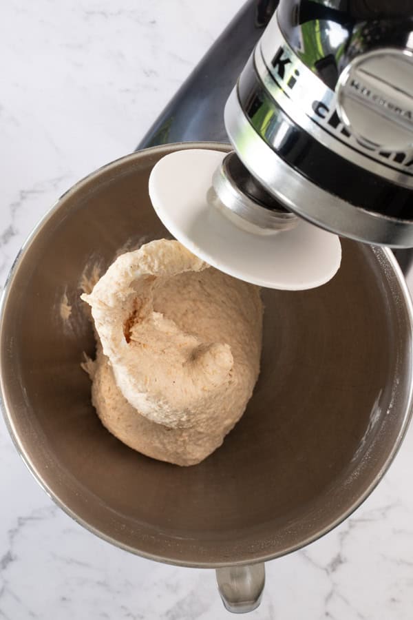 a black stand mixer, viewed from above, with a ball of mixed bread dough and the dough hook visible in the bowl. 