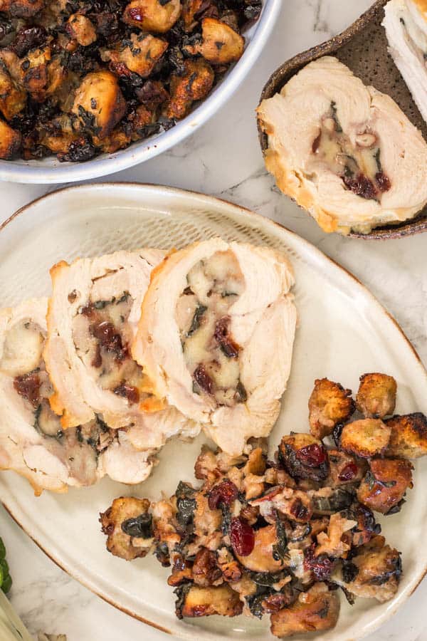 An oval platter with slices of rolled, stuffed and roasted turkey breast with cranberry pecan stuffing. 
