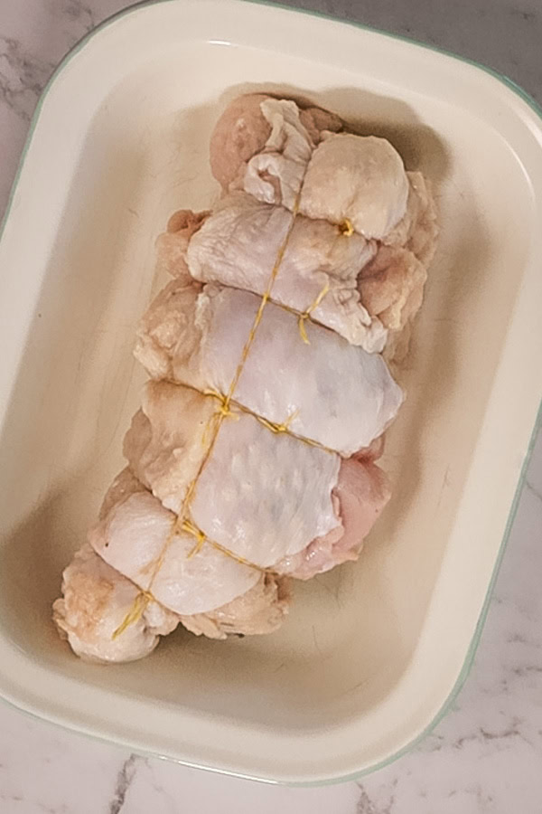 A rolled and tied turkey breast, ready to roast in an enamel baking dish.