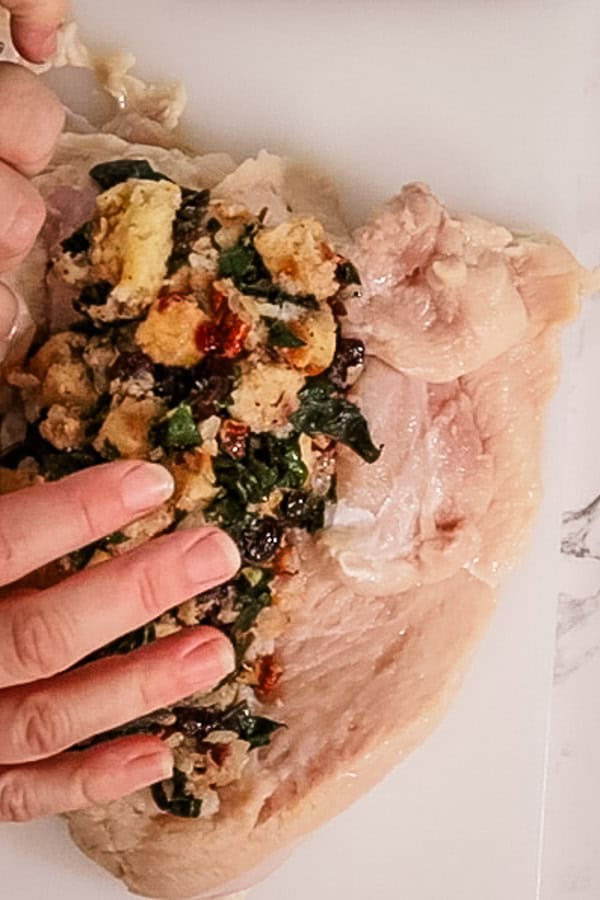 Two hands put cranberry stuffing onto a turkey breasts, ready to roll and tie for cooking.