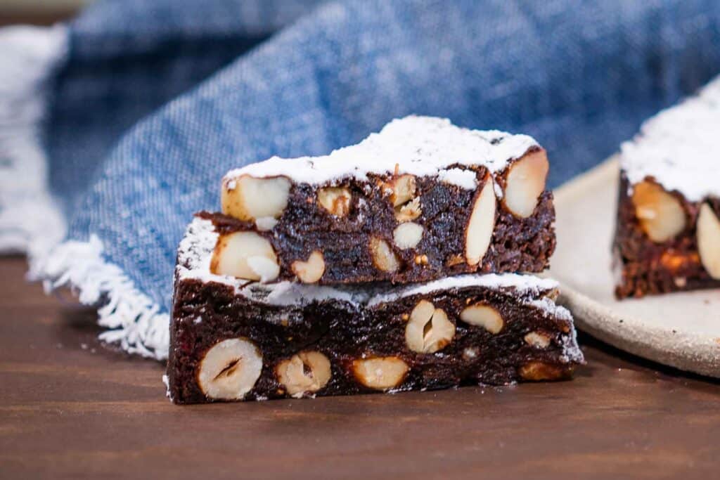 Two slices of chocolate panforte with nuts, stacked on top of each other, on a wooden surface.